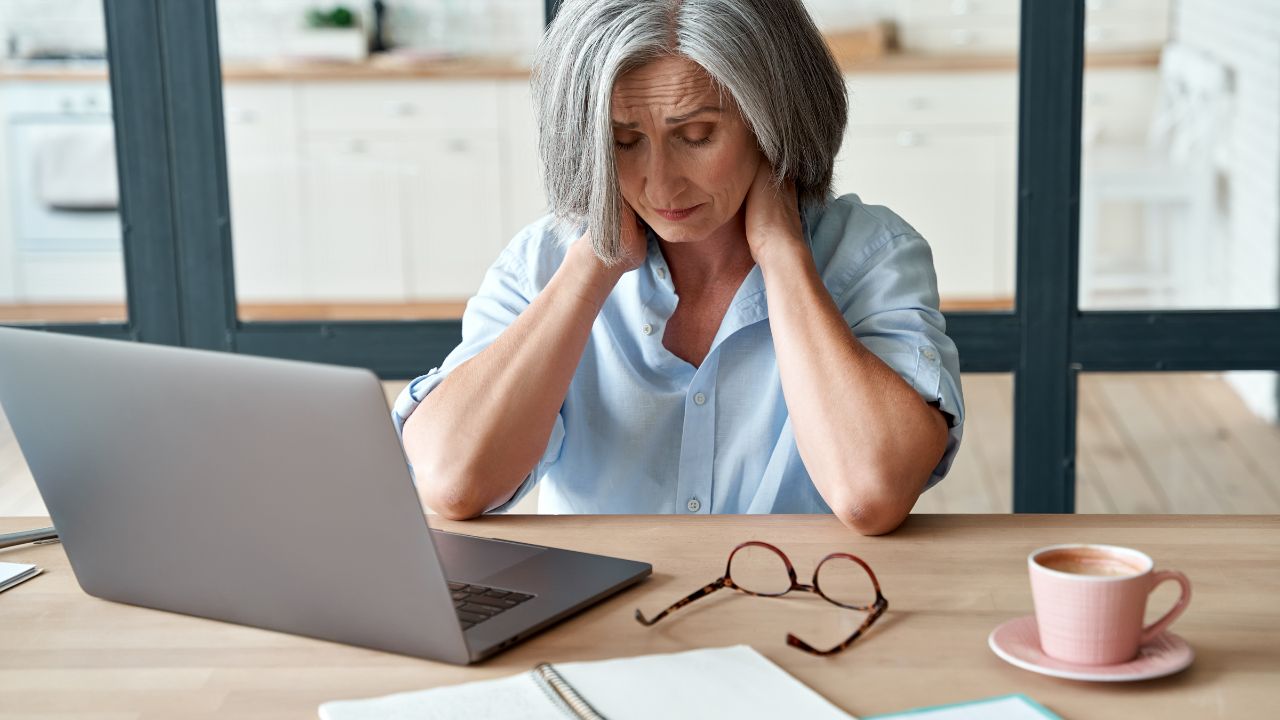 image of a woman sitting in front of a laptop computer holding her neck in pain