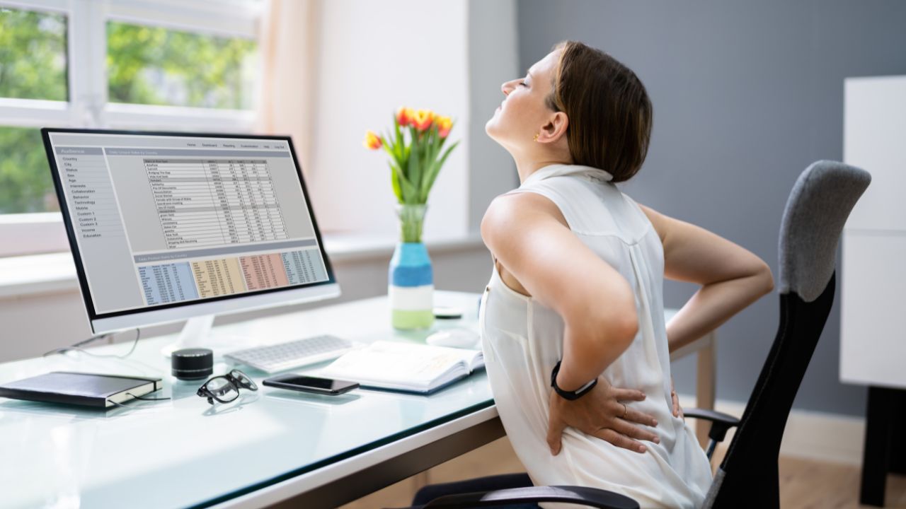 image of woman sitting in front of a computer holding her back with back pain